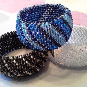 May include: Three beaded bracelets in shades of blue, black, and clear. The blue bracelet features a gradient of dark to light blue beads. The black bracelet has dark beads, and the clear bracelet has iridescent beads.