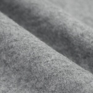Könnte beinhalten: Nahaufnahme eines weichen, grauen Stoffes mit strukturierter Oberfläche. Das Material ist gefaltet und erzeugt sanfte Kurven und Schatten. Der Stoff scheint ein mittelschweres Material zu sein, möglicherweise Wolle oder eine Wollmischung.