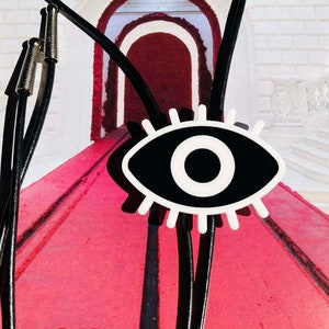 May include: A pair of black leather bolo ties with silver tips and a black and white eye design charm.