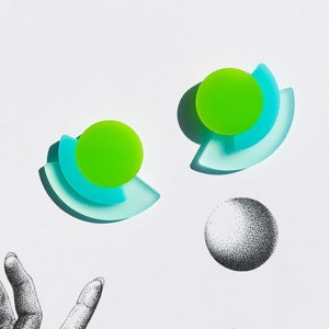 May include: A pair of green and blue acrylic earrings with a geometric design. The earrings are shaped like a crescent moon with a circle in the center.