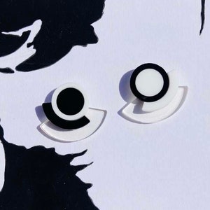 May include: A pair of black and white geometric earrings. Each earring features a white semi-circle with a black circle inside. The semi-circles are layered on top of each other.