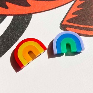 May include: Two rainbow-shaped earrings, one with red, orange, yellow, and a light orange centre, and the other with blue, green, and a light green centre.