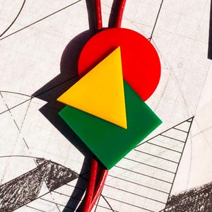 May include: A colorful bolo tie featuring geometric shapes. A red circle, yellow triangle, and green square are stacked on top of each other. The tie has a red cord. The background has a sketched design.