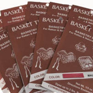 May include: A stack of mauve-colored "Basket Tree" dye packets for rattan and natural fibers. Each packet features the text "Basketry Dye" and illustrations of baskets. The packets are displayed against a white background.