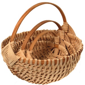 May include: Three woven baskets with wooden handles. The baskets are nested inside each other, with the largest basket on the bottom and the smallest basket on top.