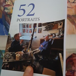 May include: A white book with the title "52 Portraits" and the author's name "Andrew Bylo" on the cover. The book features a photo of an artist's studio with two people in the photo.