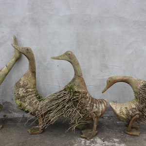 May include: Three wooden duck sculptures with a rustic, weathered finish. Each duck is decorated with natural twigs and branches, creating a unique and whimsical look.