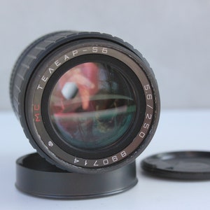 May include: A black camera lens with the text "MC Telear-S 5.6/250 8.6 0.7 1.4" printed on the side.