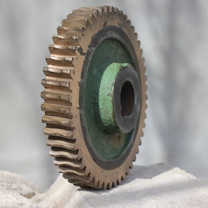 Può includere: Un grande ingranaggio dorato con un centro verde e un mozzo in metallo nero. L'ingranaggio ha un gran numero di denti ed è fatto di metallo.