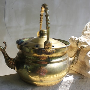 Peut inclure: Une théière vintage en laiton avec un couvercle à charnière et une poignée. La théière présente des becs en forme de cygne et une poignée détaillée. Le laiton a une teinte dorée chaude, et la théière est posée sur un fond neutre.