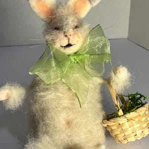 May include: A white felt bunny with a green bow and a small wicker basket filled with green moss.