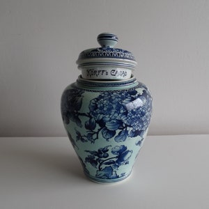 Pode incluir: Um pote de porcelana azul e branco com tampa. O pote tem um desenho floral e o texto "Korf's Cacao" na tampa.