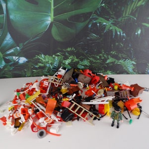 May include: A large pile of colorful plastic toy pieces, including ladders, chairs, and other assorted items. A small deer figurine and a toy figure wearing a green and brown uniform are also visible.