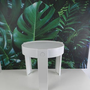 May include: White round side table with a simple design. The table has a white top and three white legs.