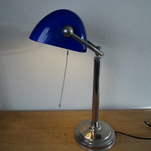 May include: A chrome desk lamp with a blue glass shade. The lamp has a flexible arm and a chain to adjust the light.