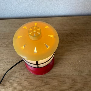 May include: A small, yellow and red table lamp shaped like a lighthouse with a black cord.
