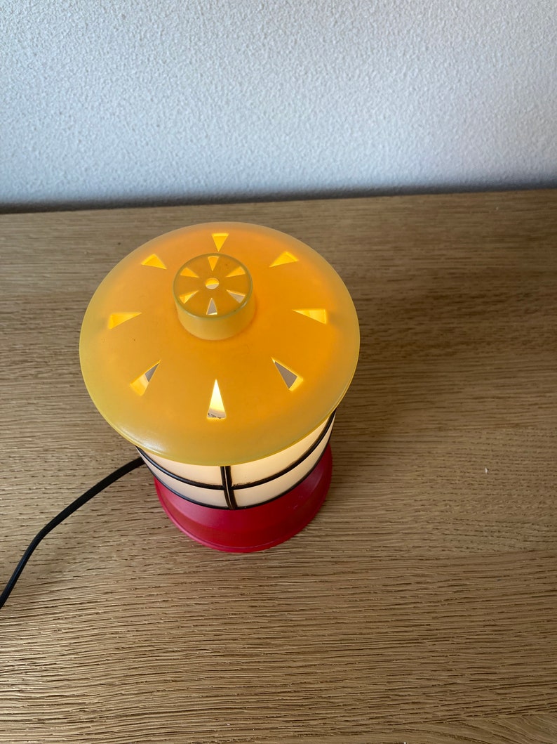 May include: A small, yellow and red table lamp shaped like a lighthouse with a black cord.