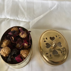 Peut inclure: Un pot-pourri en laiton avec un couvercle. Le couvercle est décoré de cœurs et de volutes. Le pot-pourri est rempli de fleurs et de feuilles séchées.
