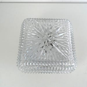 Op de afbeelding: Een vierkante schaal van helder glas met een gefacetteerd, geometrisch sterpatroon op de bovenzijde en een getextureerd diamantgeslepen ontwerp langs de zijkanten. Het glas is transparant en reflecteert licht door de scherpe prismatische sneden.