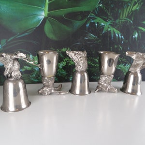 Pode incluir: Conjunto de seis copos de shot de prata com desenhos de cabeça de animal. Cada copo apresenta um animal diferente, incluindo um veado, um javali e um cavalo. Os copos são todos do mesmo estilo, com uma base em forma de sino e uma taça que tem a forma de uma cabeça de animal.