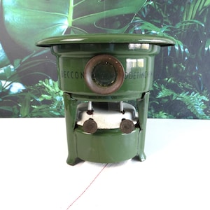 May include: A vintage green enamelled metal stove with a circular viewing window, featuring the text BECCON DOETINCHEM and MADE IN HOLLAND printed on the front. The stove has a white burner component and two small circular knobs.