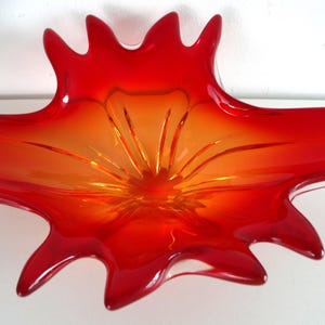 Könnte beinhalten: Eine lebendige, abstrakte Glasschale in Rot- und Orangetönen. Die Schale hat ein Sternmuster mit länglichen, spitzen Kanten. Die Mitte ist hellorange, das zu einem tiefen Rot an den Spitzen übergeht, was einen auffälligen visuellen Effekt erzeugt.