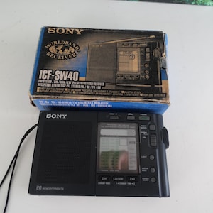 Puede incluir: Un receptor de radio de banda mundial Sony ICF-SW40 negro con una pantalla digital y 20 presintonías de memoria. El receptor está en su caja original, que es azul y blanca con el logotipo de Sony y el nombre del producto.
