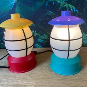 May include: Two decorative table lamps with a cage design. The lamp on the left has a yellow top and a red base. The lamp on the right has a purple top and a teal base.