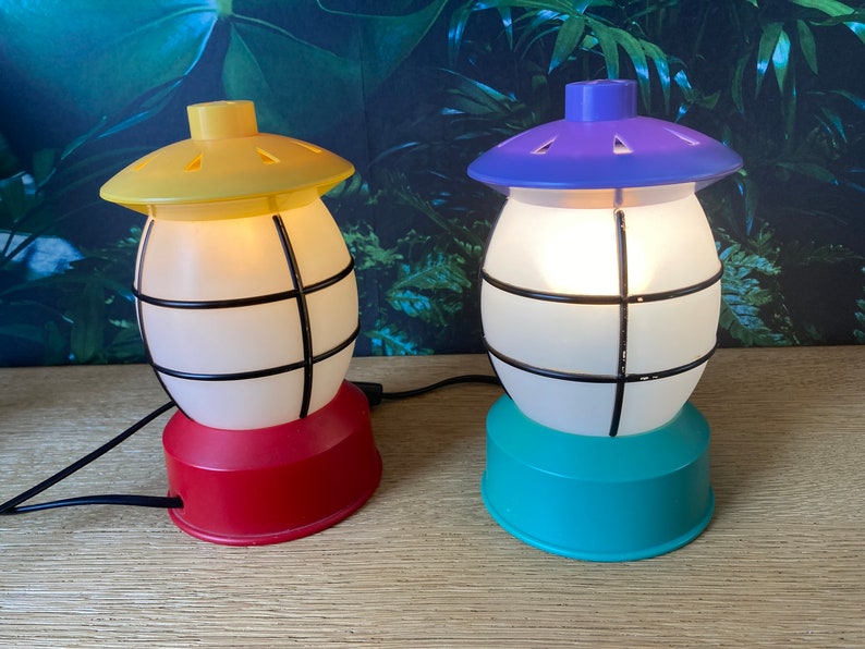 May include: Two decorative table lamps with a cage design. The lamp on the left has a yellow top and a red base. The lamp on the right has a purple top and a teal base.