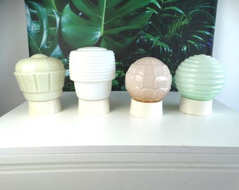 May include: Four glass lamp shades with white bases. The first is pale green with vertical panels, the second is white with horizontal ridges, the third is a spherical peach shade with a grid pattern, and the fourth is a pale green ribbed sphere.