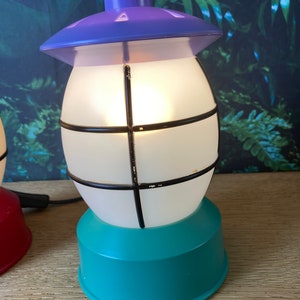 May include: A purple and teal table lamp shaped like a lantern with a white frosted glass shade and black metal accents.