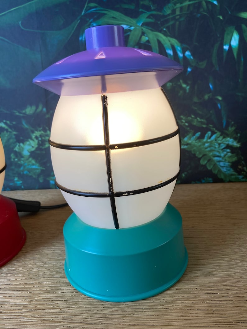 May include: A purple and teal table lamp shaped like a lantern with a white frosted glass shade and black metal accents.