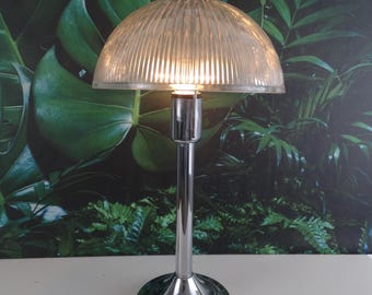 Peut inclure: Une lampe de table en chrome avec un abat-jour en verre cannelé transparent. La lampe a un design simple et un look classique.