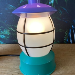 May include: A teal and purple table lamp shaped like a lantern with a white frosted glass shade and a black wire cage.