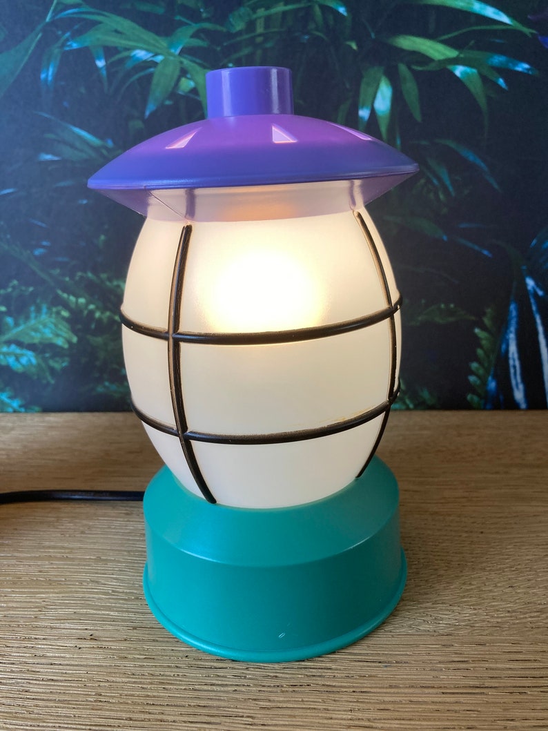 May include: A teal and purple table lamp shaped like a lantern with a white frosted glass shade and a black wire cage.
