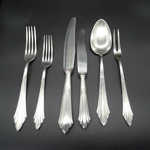 Può includere: Un set di sei posate in argento placcato, tra cui un coltello, una forchetta, un cucchiaio e due forchette più piccole. I manici sono decorati e presentano un motivo floreale.