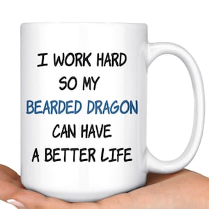 Puede incluir: Taza de cerámica blanca con una inscripción en negro y azul que dice "Trabajo duro para que mi dragón barbudo pueda tener una vida mejor."