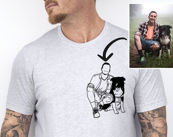 May include: A gray t-shirt with a black and white illustration of a person with a dog. The illustration is on the front of the shirt. The shirt is being modeled by a person with tattoos on their arms. The text "Color: Ash" is visible in the bottom right corner of the image.