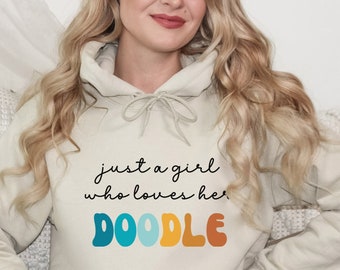 Può includere: Una felpa con cappuccio beige chiaro con una grafica che dice "Just a girl who loves her DOODLE" in lettere colorate in stile retrò.