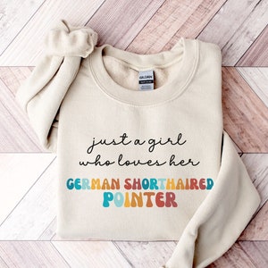 May include: A beige sweatshirt with the text "just a girl who loves her GERMAN SHORTHAIRED POINTER" in colourful, retro-style lettering.