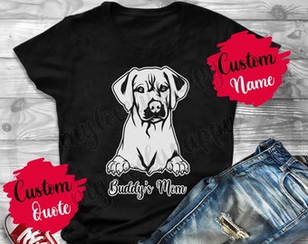 May include: Black t-shirt with a white outline of a Labrador Retriever dog and the text "Buddy's Mom". The shirt is laying on a pair of blue jeans and red sneakers.