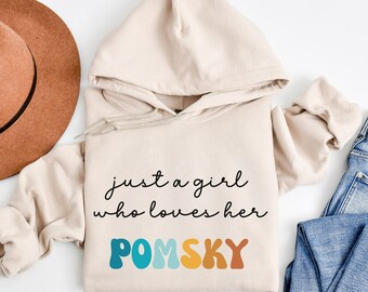 May include: A beige hoodie with a hood and long sleeves. The hoodie has the text "just a girl who loves her POMSKY" printed on the front in black and colorful letters.
