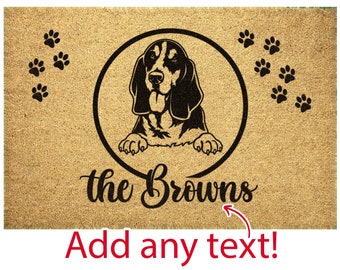 May include: A brown doormat with the text "the Browns" and a black and white illustration of a Bloodhound dog inside a circle.  There are paw prints around the circle.