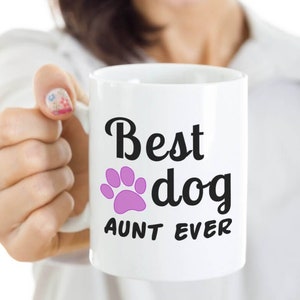 May include: White ceramic coffee mug with black text that reads "Best dog aunt ever" and a pink paw print.