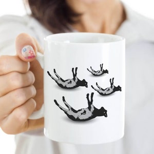 May include: White ceramic mug with a black and white graphic of four sheep falling from the sky.