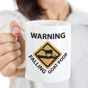 Puede incluir: Taza de caf&eacute; de cer&aacute;mica blanca con una se&ntilde;al de advertencia negra que dice "WARNING FALLING GOAT POOP" con una imagen de dibujos animados de una cabra defecando.