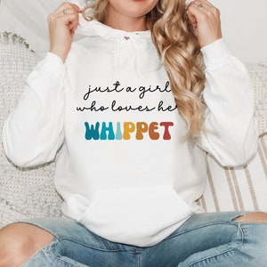 Może przedstawiać: Biała bluza z kapturem z napisem "just a girl who loves her WHIPPET" w czarnym kolorze i słowem "WHIPPET" w tęczowych kolorach.