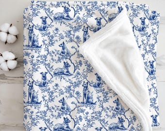 May include: A white and blue blanket with a dog and floral pattern. The blanket features a repeating design of dogs in various poses amidst a floral motif. The reverse side is a soft, white plush material.