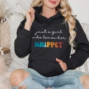Może przedstawiać: Czarna bluza z kapturem z napisem "just a girl who loves her WHIPPET" w kolorach tęczy.