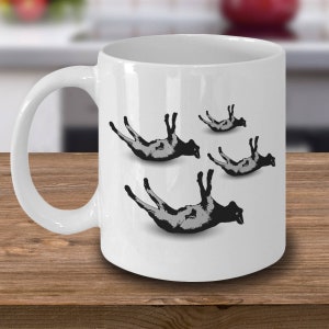 May include: White ceramic coffee mug with a black and white illustration of four sheep upside down on the front.